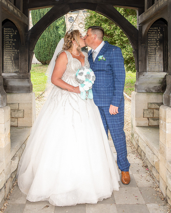 Bride and groom kissing beneath a stone church arch during their Wiltshire wedding.